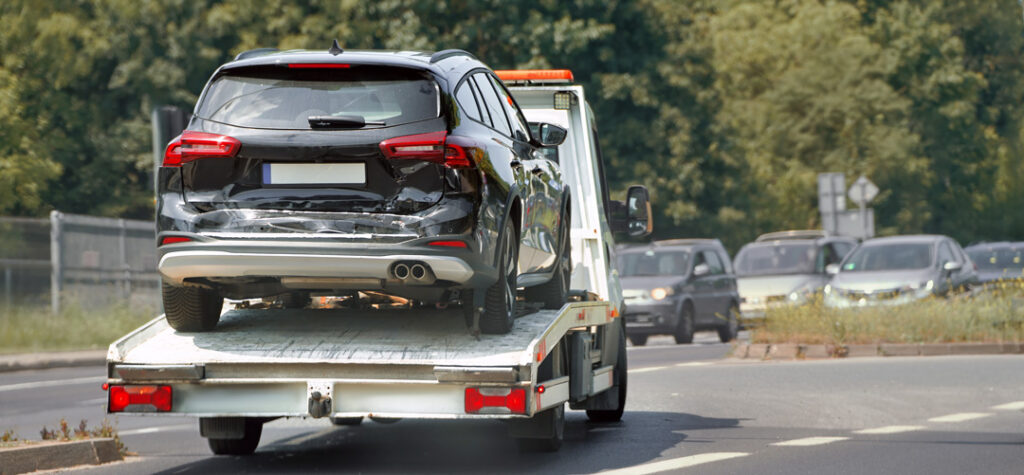 Damaged black car being transported on tow truck after accident