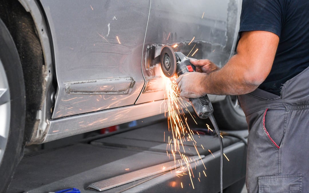 Panel beater using angle grinder on car body at Steve Koulis Smash Repairs