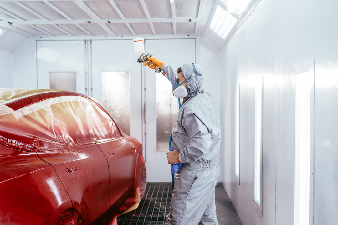 Professional car painter in Steve Koulis Smash Repairs spraying red paint on vehicle
